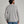 Back view of a person wearing a long sleeve light grey sweater and blue jeans against a medium grey background.