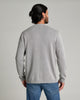 Back view of a person wearing a long sleeve light grey sweater and blue jeans against a medium grey background.