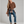 Person wearing a brown sweater that has buttons going down 1/4 of the front of the sweater and blue jean pants and also has a brown and tan flannel tied around their waste against a light grey background.