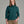 Person wearing a deep teal sweater and khaki pants against a grey background.