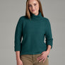 Person wearing a deep teal sweater and khaki pants against a grey background.
