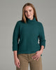 Person wearing a deep teal sweater and khaki pants against a grey background.