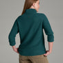 Person wearing a deep teal sweater and khaki pants against a grey background.
