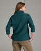 Person wearing a deep teal sweater and khaki pants against a grey background.