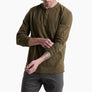 Person wearing a dark olive green long sleeve shirt with 3 buttons and grey pants against a white background.