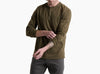 Person wearing a dark olive green long sleeve shirt with 3 buttons and grey pants against a white background.