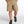 Person wearing beige shorts and green hiking shoes on a white background