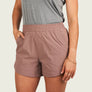 Person wearing dusty brown shorts with a grey shirt against a beige background