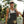 Woman wearing a cap and overalls standing outdoors with trees in the background