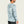 Person wearing a grey camo long sleeve with a hood on a beige background
