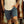 Person wearing a beige shirt and blue shorts standing in front of a rusty metal surface.