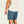 Person wearing blue shorts and a beige shirt on a plain background