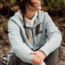 Person wearing a light blue 1/4 zip pull over sitting in nature