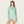Person wearing a frosty green long sleeve with a hood and a pock on the front with pale orange shorts against a blank background