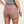 Person wearing dusty brown shorts with a pocket on the back and a grey shirt against a beige background