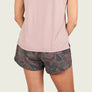 Person wearing a light pink tank top and camo shorts with a black background