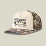 Cream and camo colored baseball cap that says Marsh Wear outfitters and has a buck on the front against a pale green background.