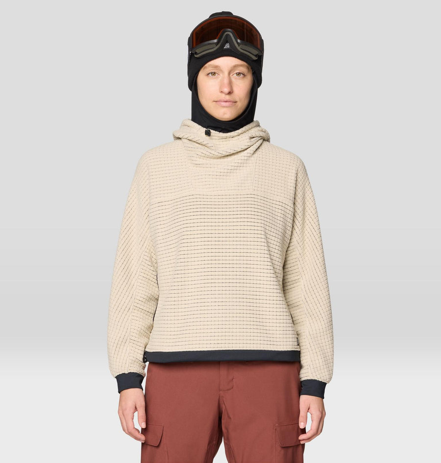 Person wearing a beige textured sweater and brown pants with a black helmet and goggles on a light gray background