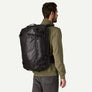Person in an olive green jacket and grey pants wearing a black backpack with a Patagonia logo in light grey on the side.