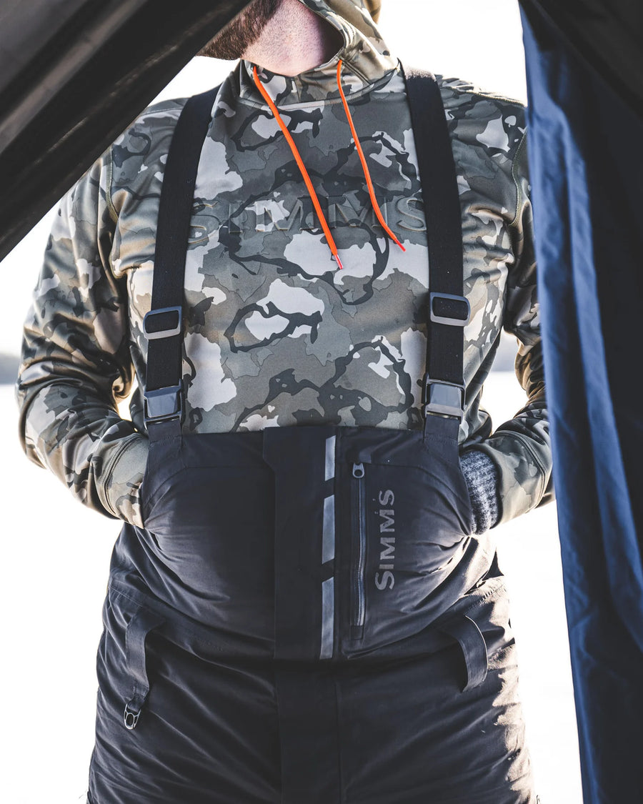 Person wearing camouflage jacket and black suspenders with 'Simms' branding.