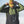 Person wearing a green jacket, black overalls, and a yellow cap with a logo against a clear sky.