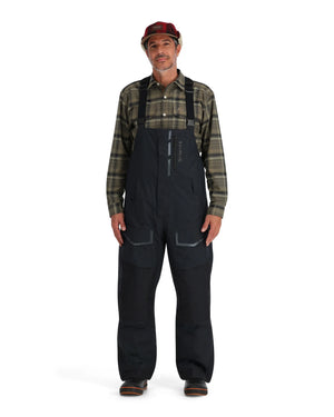 Man wearing black Simms Challenger bibs and a plaid shirt on a white background