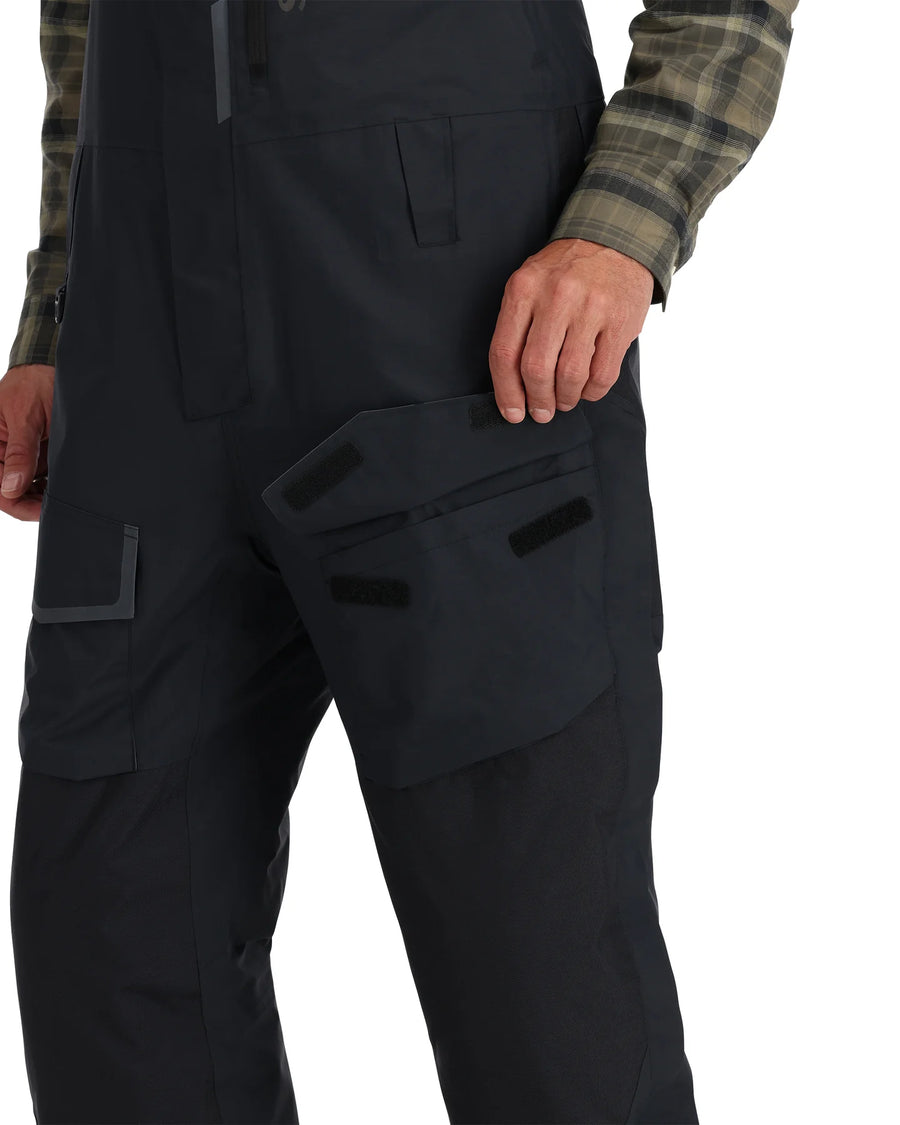 Black Simms Challenger Insulated bibs with multiple pockets worn by a person on a white background
