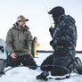 Two men ice fishing on a frozen lake with one holding a fish wearing Simms Challenger Jackets