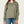 Person wearing a sage green 1/4 button long sleeve with blue jeans against a white background.