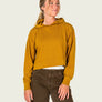 Person wearing a mustard yellow cropped hoodie with brown pants against a white background.
