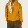 Back view of a person wearing a cropped mustard orange hoody with brown pants against a white background.