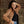 Woman wearing a brown jacket and blue jeans against a brick wall.