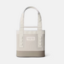 A Tote bag that is cream, beige and a light tan color with the Yeti logo on the front in same cream color as the handles of the bag.