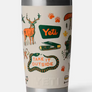 Tan Yeti cup with the yeti logo on it and camping images all over it in a green orange and yellow color way against a white background.