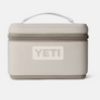 Light tan insulated snack box with darker tan accents that has the Yeti logo on the front of it.