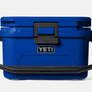 Front view of a Yeti hard cooler that is blue and has the Yeti logo on the from with a large handle for carrying against a white background.