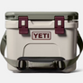 light tan, maroon and pale dark green cooler that has a Yeti logo on the front of it as well as an over the shoulder strap.