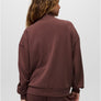 Back view of a person wearing a dark maroon colored sweatshirt with the same color sweatpants against a grey background.